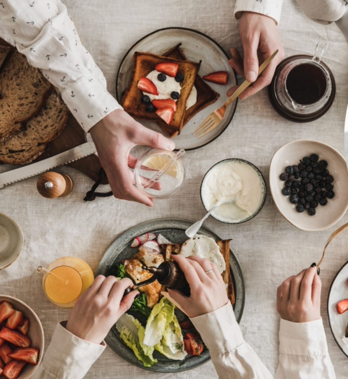 An overhead Mediterranean breakfast table with wholegrain toast, yoghurt, berries, eggs and olive oil